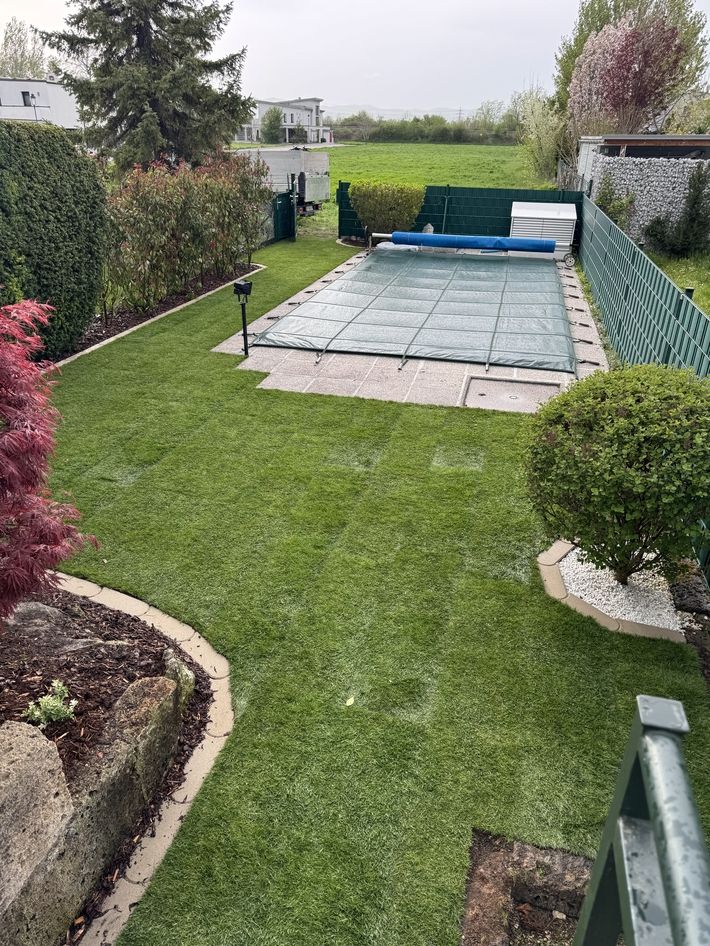 Garten mit rechteckigem, abgedecktem Pool, umgeben von Rasenflächen, Hecken und einem Baum im Hintergrund